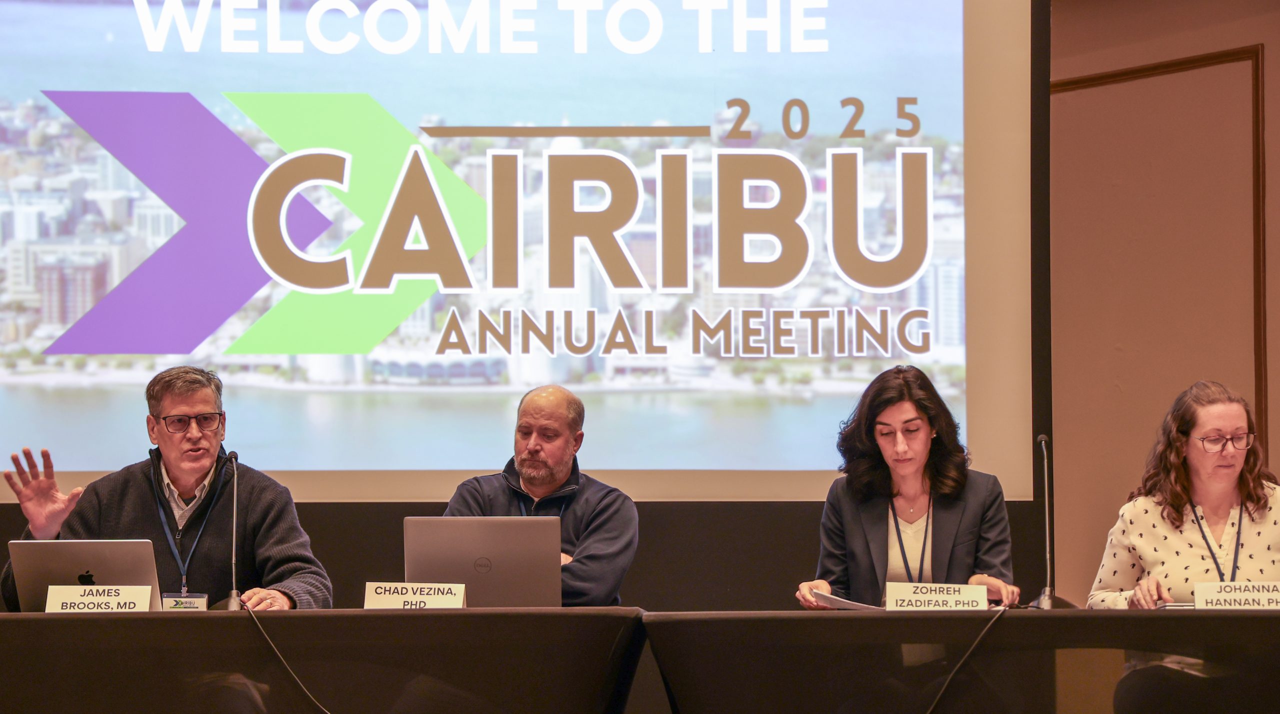 Three panelists sitting in front of CAIRIBU Annual Meeting picture